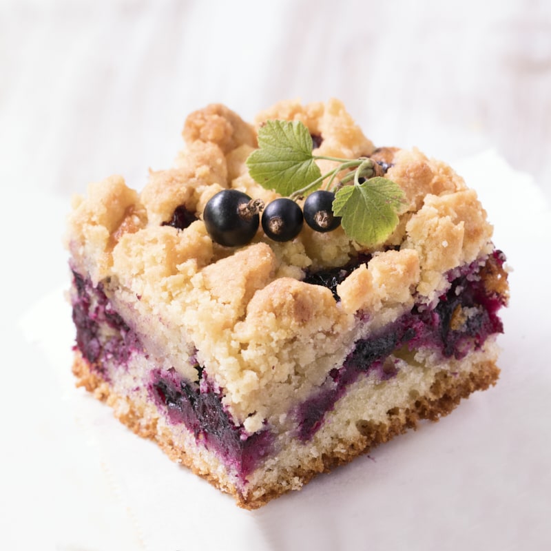 Une part de crumb cake au cassis présentée sur du papier sulfurisé blanc