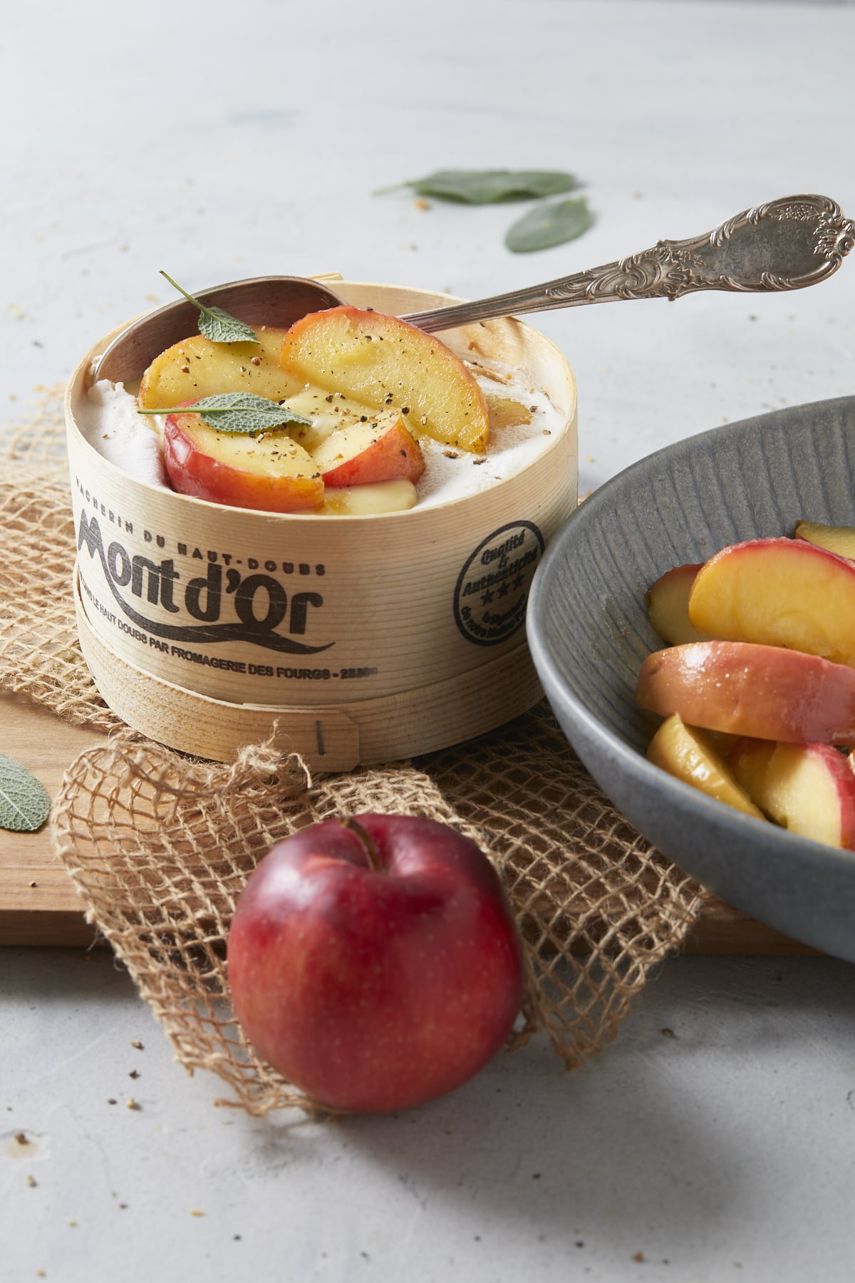Mont d'Or aux pommes servi chaud dans sa boîte en épicéa et une assiette de pommes fondantes au miel.