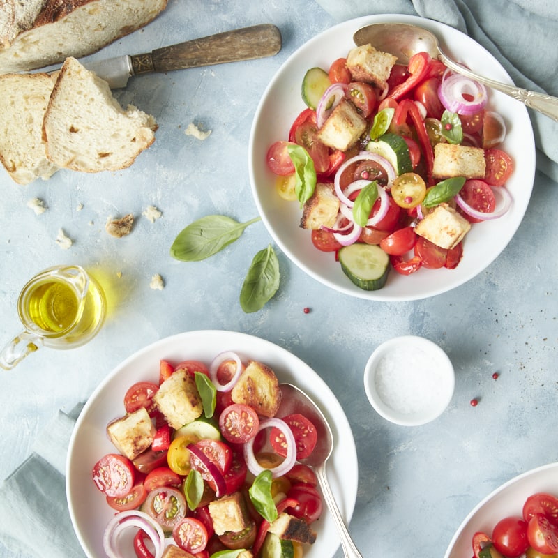 Flatlay sur deux assiettes de panzanella, accompagnées d'huile d'olive et de pain.