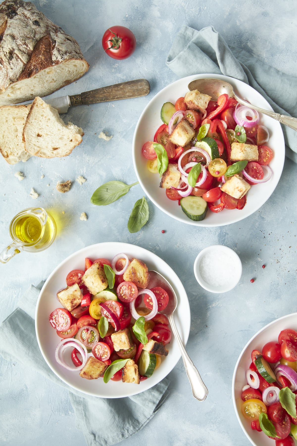 Flatlay sur trois assiettes de panzanella, accompagnées d'huile d'olive et de pain.