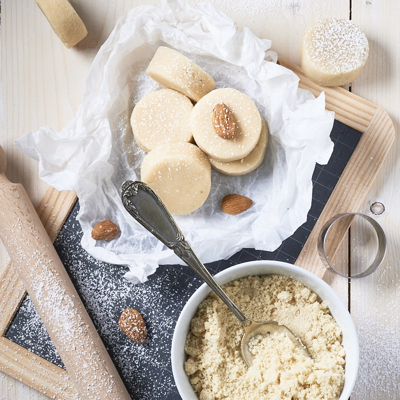 Des pâtes d'amande faites maison, posées sur une petite ardoise d'écolier et accompagnée d'un petit rouleau à pâtisserie pour enfants.