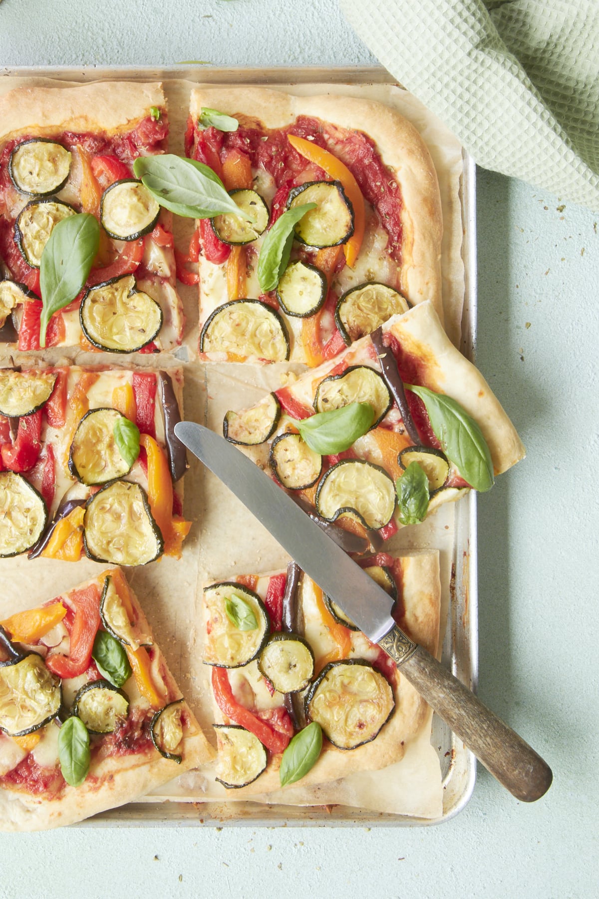 Pizza aux légumes grillés, découpée en parts et présentée sur une plaque de cuisson.