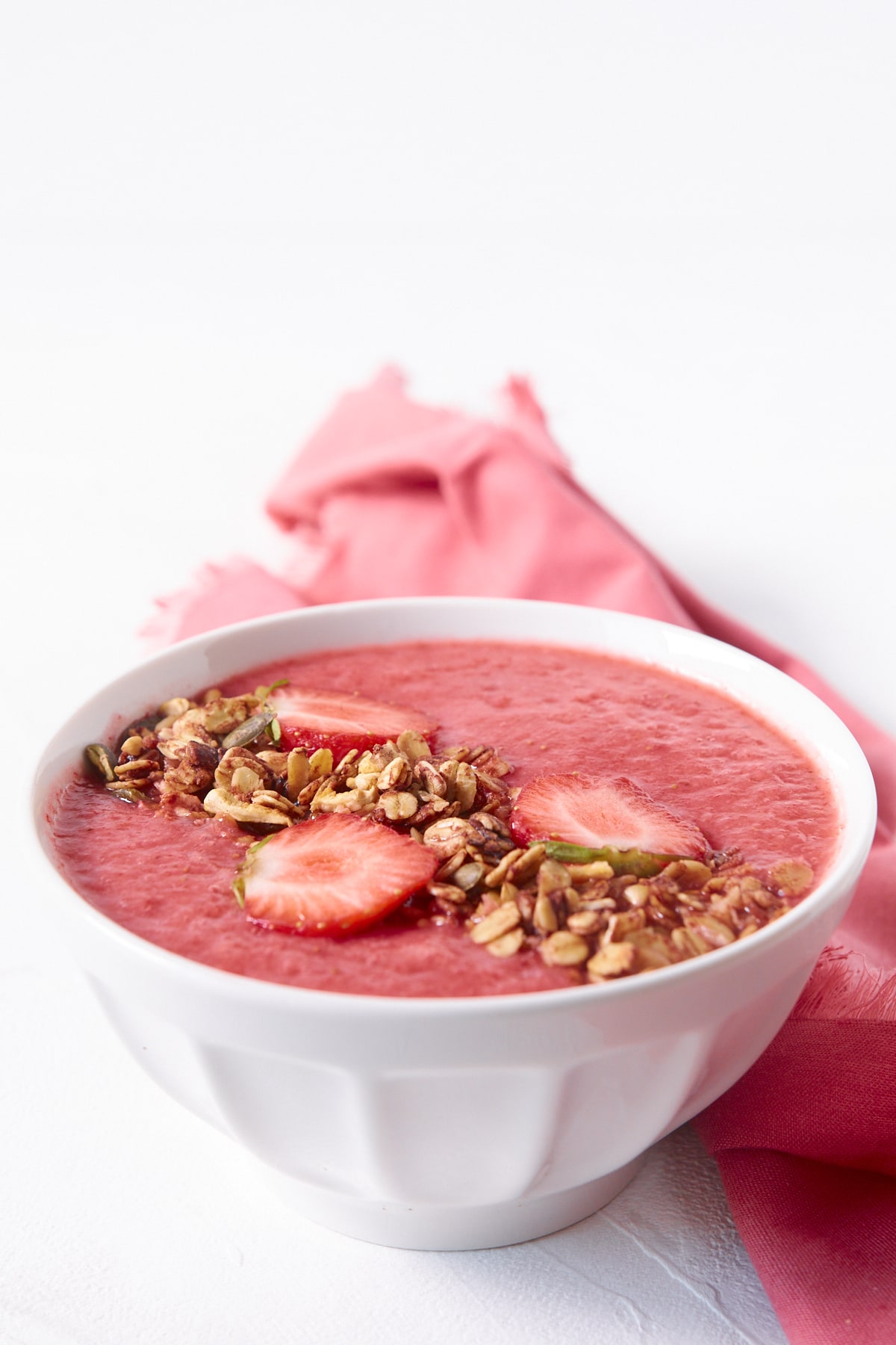 Gros plan sur un bol de smoothie banane fraises décoré de granola et de quelques tranches de fraises.