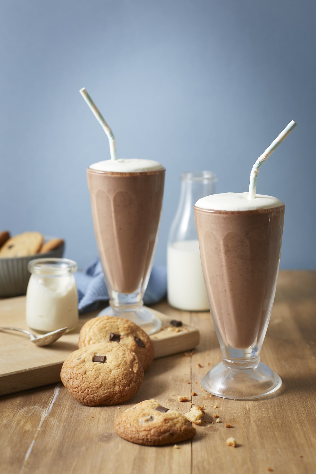 Deux smoothies, décorés de crème fouettée, avec leurs pailles et accompagnés de cookies au chocolat.