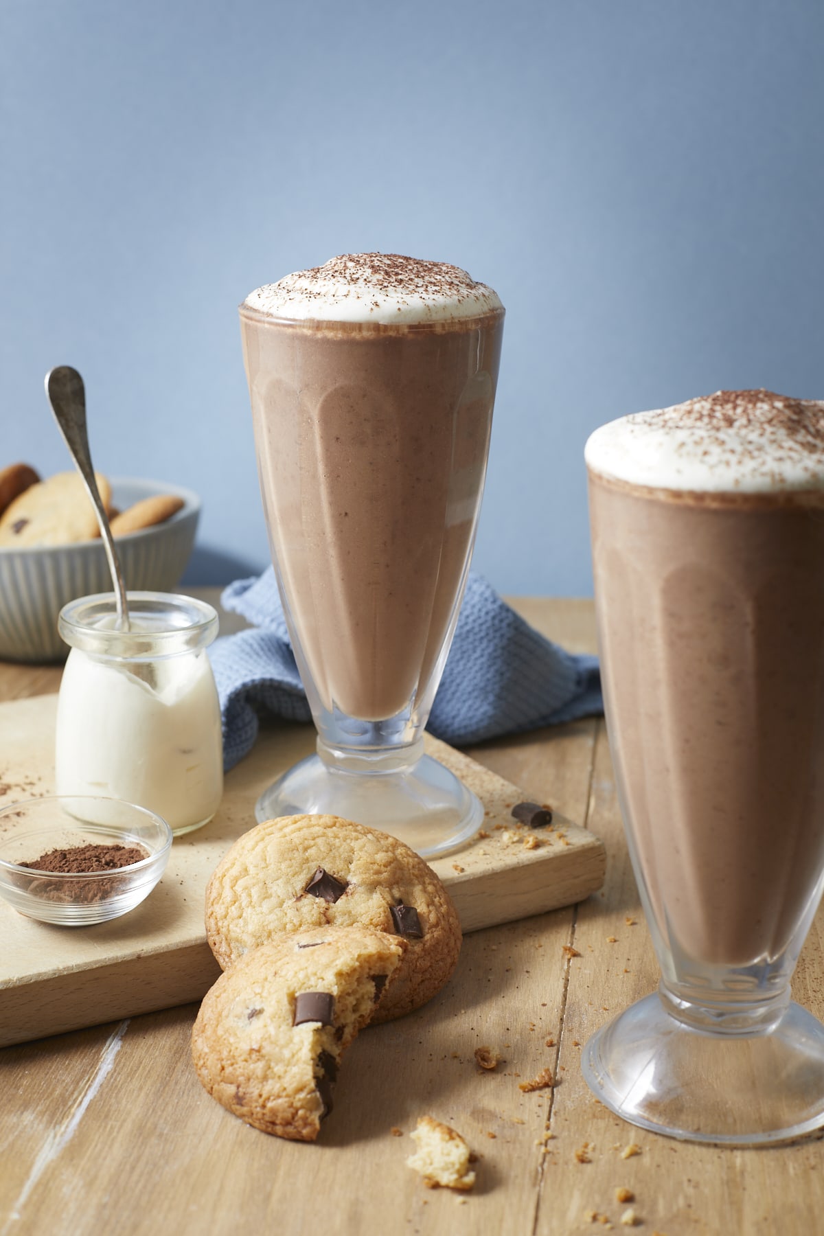 Deux smoothies, décorés de crème fouettée et saupoudrés de cacao, accompagnés de cookies au chocolat.