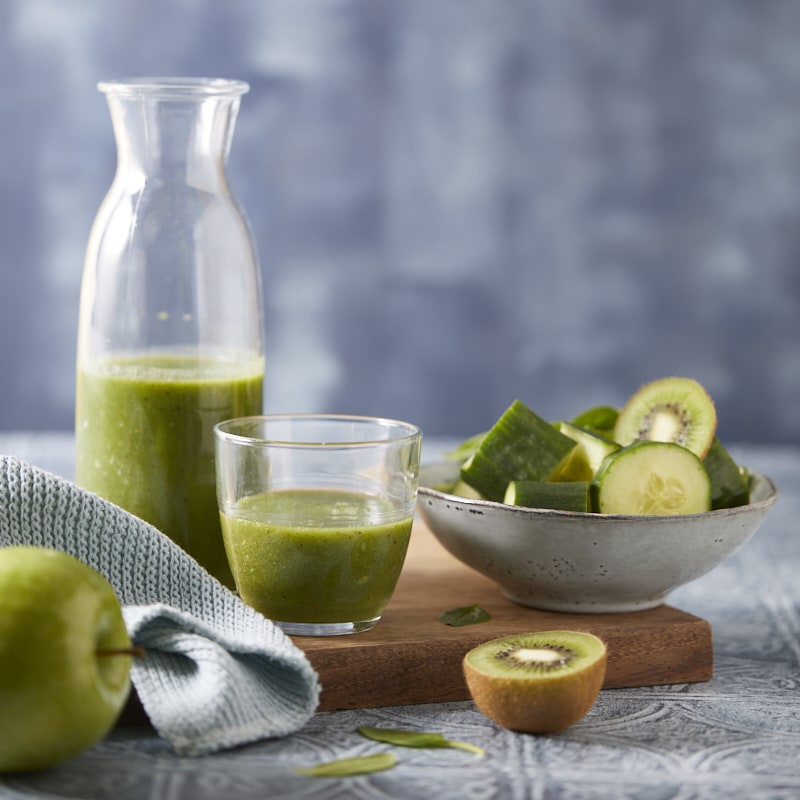 Smoothie vert à la pomme, au concombre, au kiwi et aux épinards servi dans un verre avec ses ingrédients frais