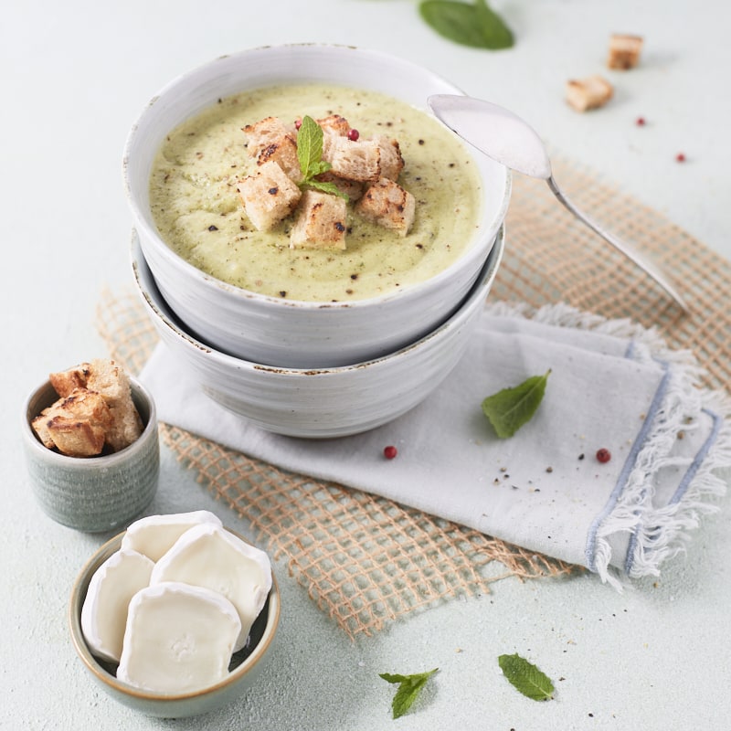 Plan rapproché sur un bol de soupe de courgettes à la menthe, garni de croûtons.