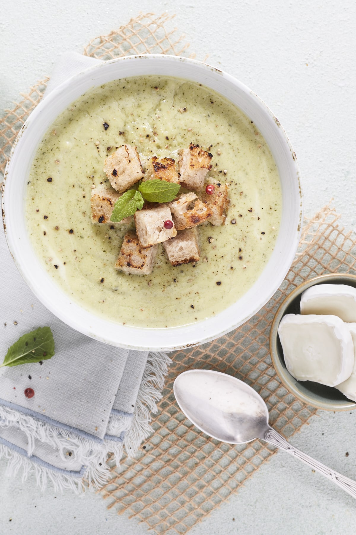 Gros plan en flatlay sur un bol de soupe de courgettes à la menthe, garni de croûtons.