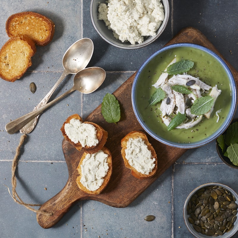 Soupe verte de brocoli servie dans un bol, garnie de poulet et de feuilles de menthe.