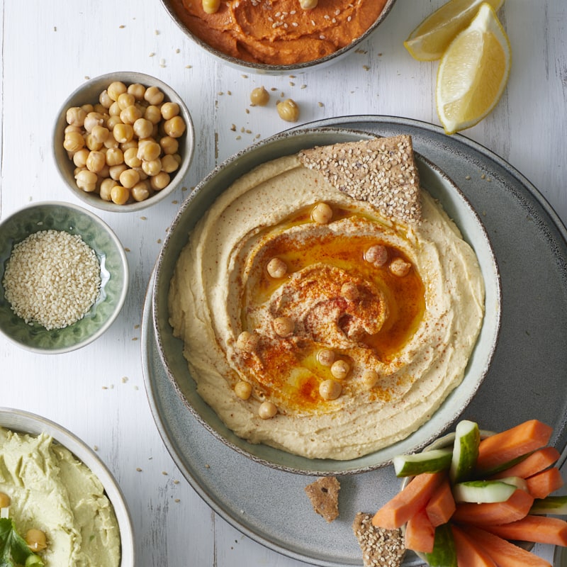 Trio de houmous maison présenté dans trois bols avec légumes croquants et crackers au sésame.