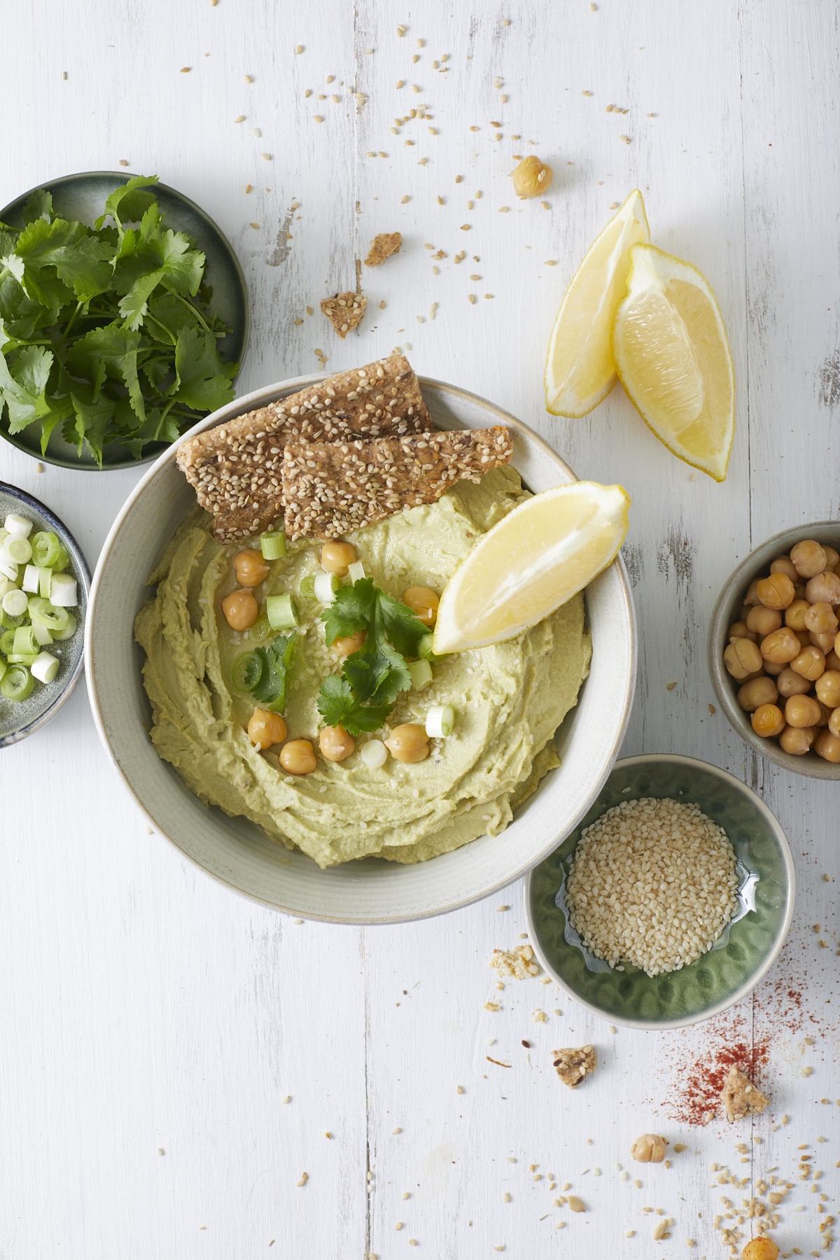 Un bol de houmous à l'avocat accompagné de crackers et de garnitures.