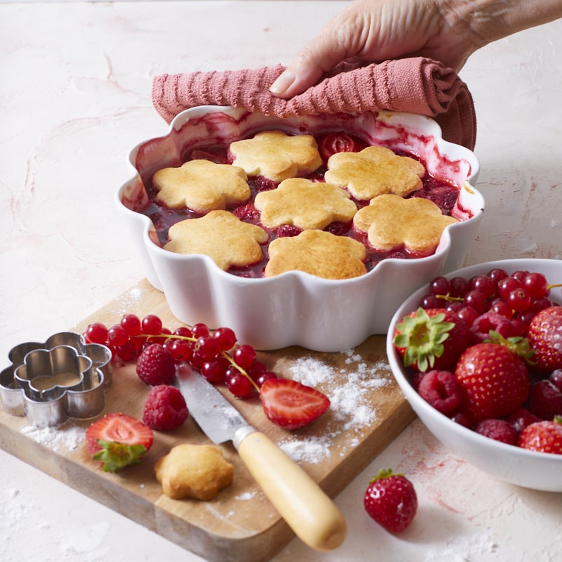Cobbler au fruits rouges tout juste sorti du four, avec à côté du plat, des fraises, groseilles et framboises