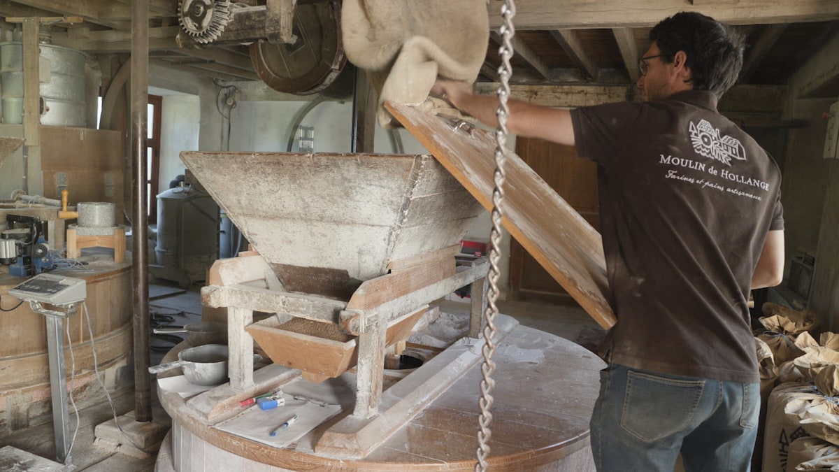 Le meunier ôte le couvercle de la meule pour y verser des grains de froment.