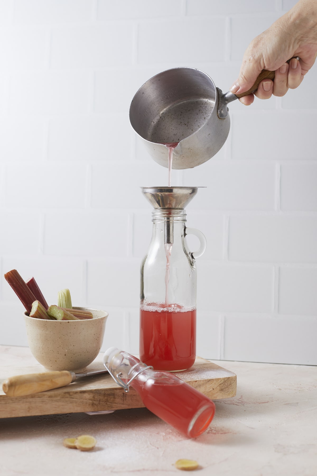 Du sirop de rhubarbe au gingembre est versé dans une bouteille via un entonnoir.