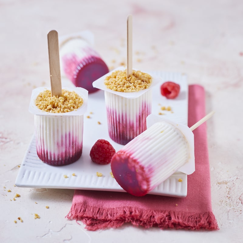 Quatre petits Suisses glacés, façon cheesecake à la framboise sur un petit plat de céramique blanche et une serviette rose.
