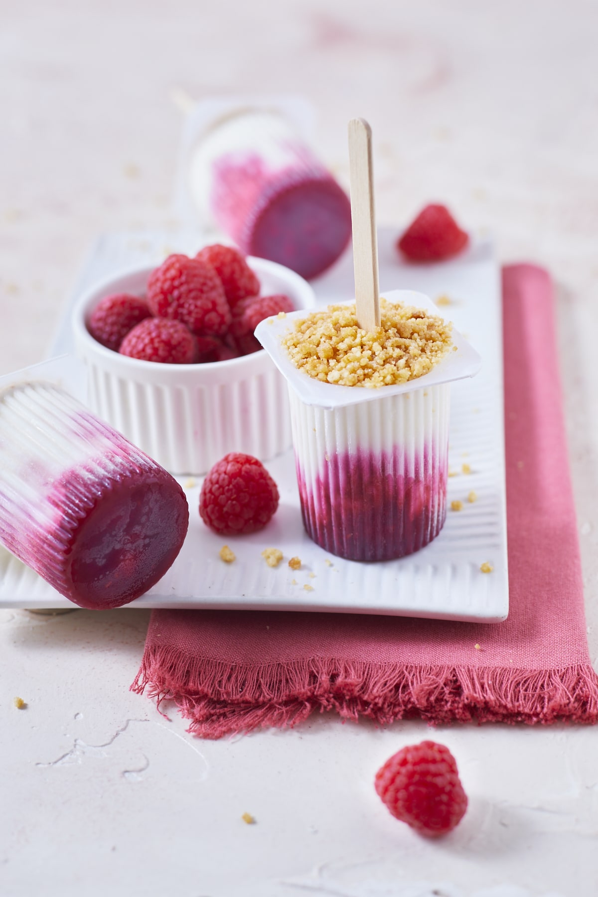 Un petit bol de framboises fraîches entourés de trois petits suisses glacés, préparés façon cheesecake à la framboise avec un émietté de galettes bretonnes.