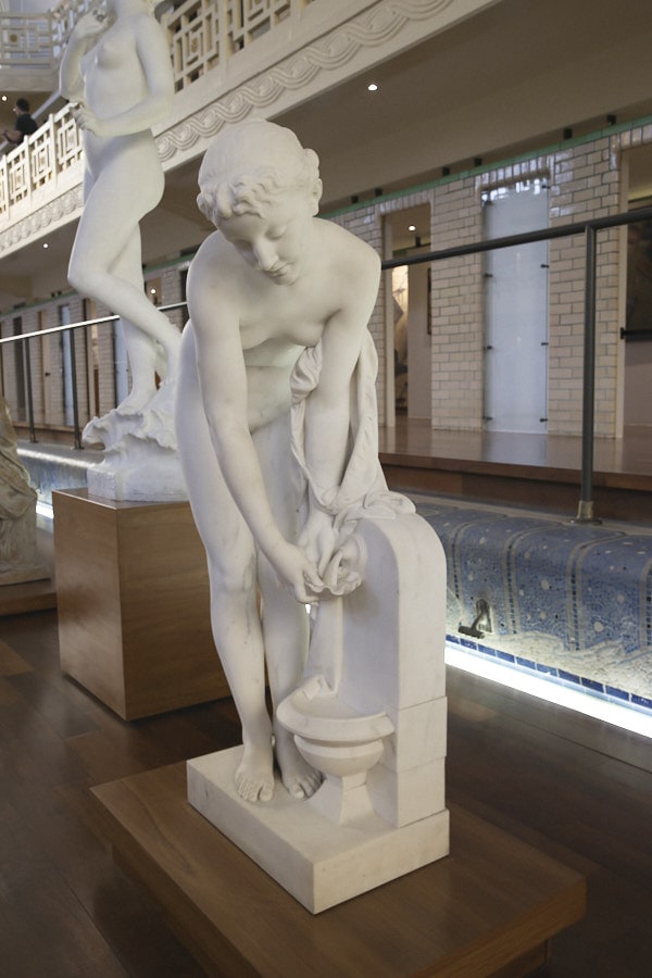 Une statue blanche de femme à la fontaine, le long de la piscine
