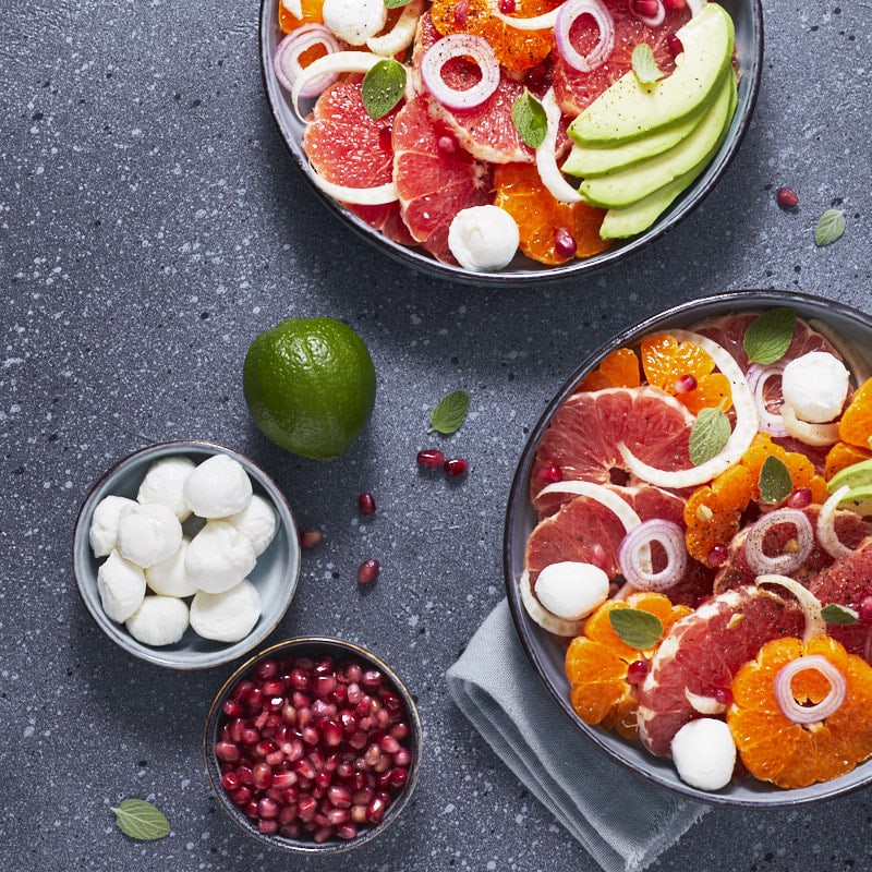 Deux assiettes de salade aux agrumes, avocat et billes de mozzarella.