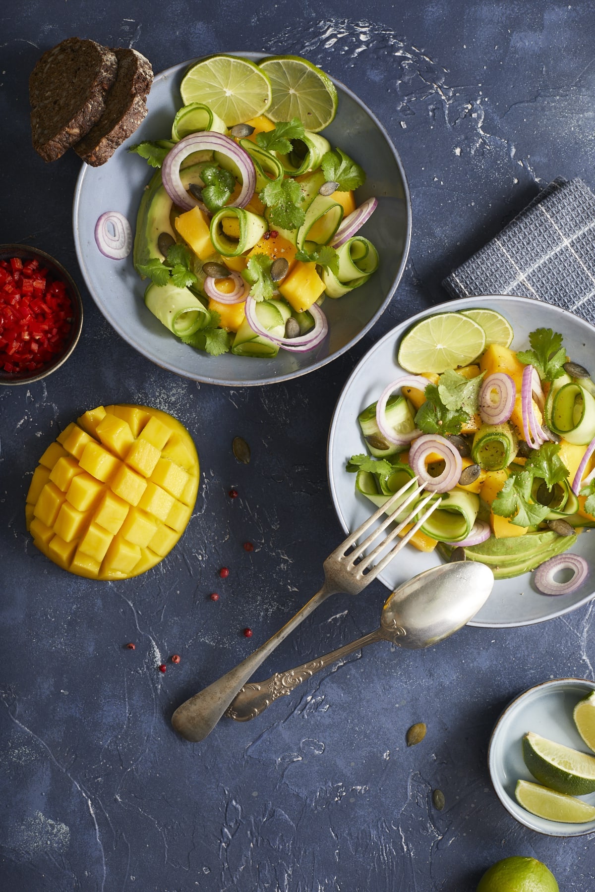Deux assiettes de salade de mangue avocats coriandre, une mangue et un petit pot de piments.