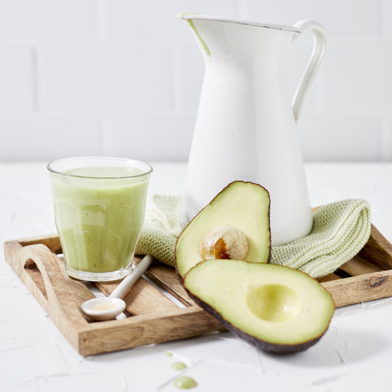 Cruche et un verre de smoothie avocat vanille avec deux moitiés d'avocat