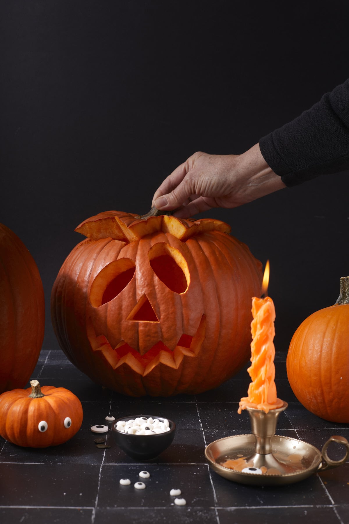 Main soulevant le couvercle de la lanterne d’Halloween, près d’une petite courge aux yeux en sucre